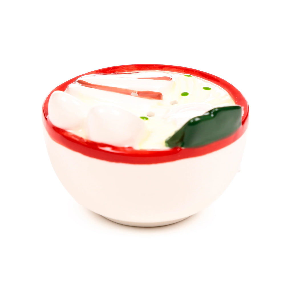 Angled view of a ceramic ramen bowl salt and pepper shaker, featuring a white bowl with a red rim, containing white noodle shapes, green specks, a dark green seaweed piece, and red strip details.