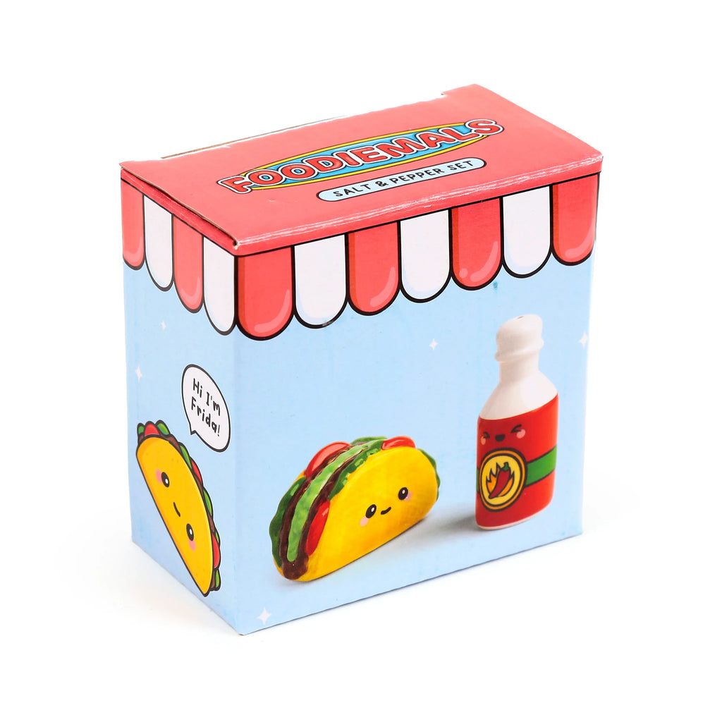 Angled view of the colourful salt and pepper set packaging, depicting a ceramic taco shaker character labelled 'Frida' and a hot sauce bottle shaker, with 'FOODIEMALS' text and a red awning design on the box top.
