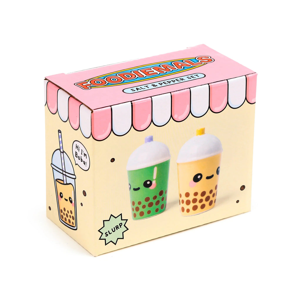Angled view of a light yellow salt & pepper set box, featuring 'Foodiemals' branding and a pink awning design on its top. The box front displays illustrations of a green matcha and a yellow boba bubble tea character, while the side shows a larger boba cup illustration.