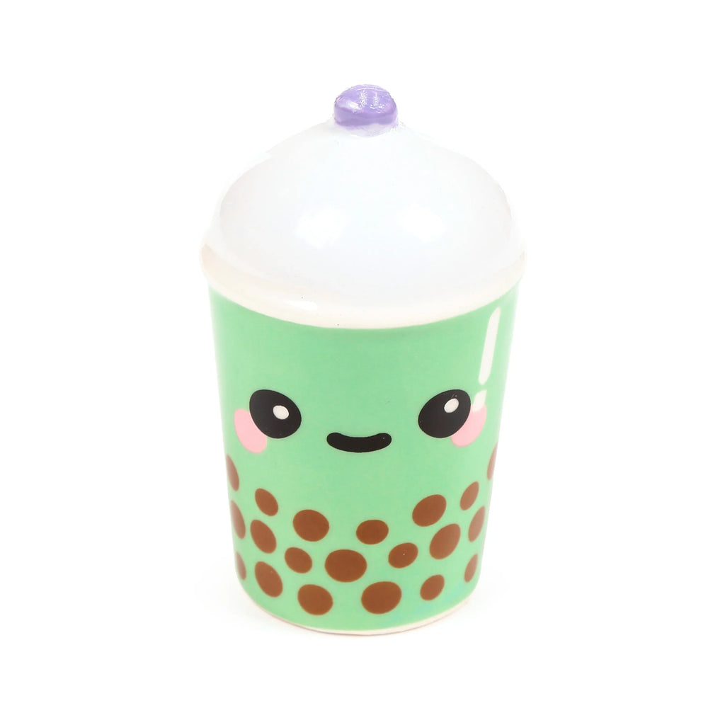 Front view of a ceramic matcha bubble tea shaker, featuring a cute cartoon face with pink cheeks, a light green body with brown boba dots, a white domed lid, and a purple straw detail.