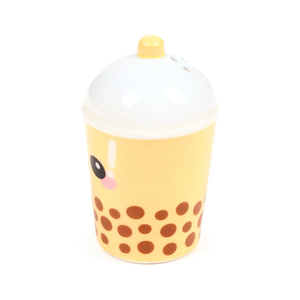 Front view of a pale yellow ceramic boba bubble tea shaker with brown boba patterns, a white domed lid, light yellow straw, and a cartoon eye with a pink cheek, shown on a white background.
