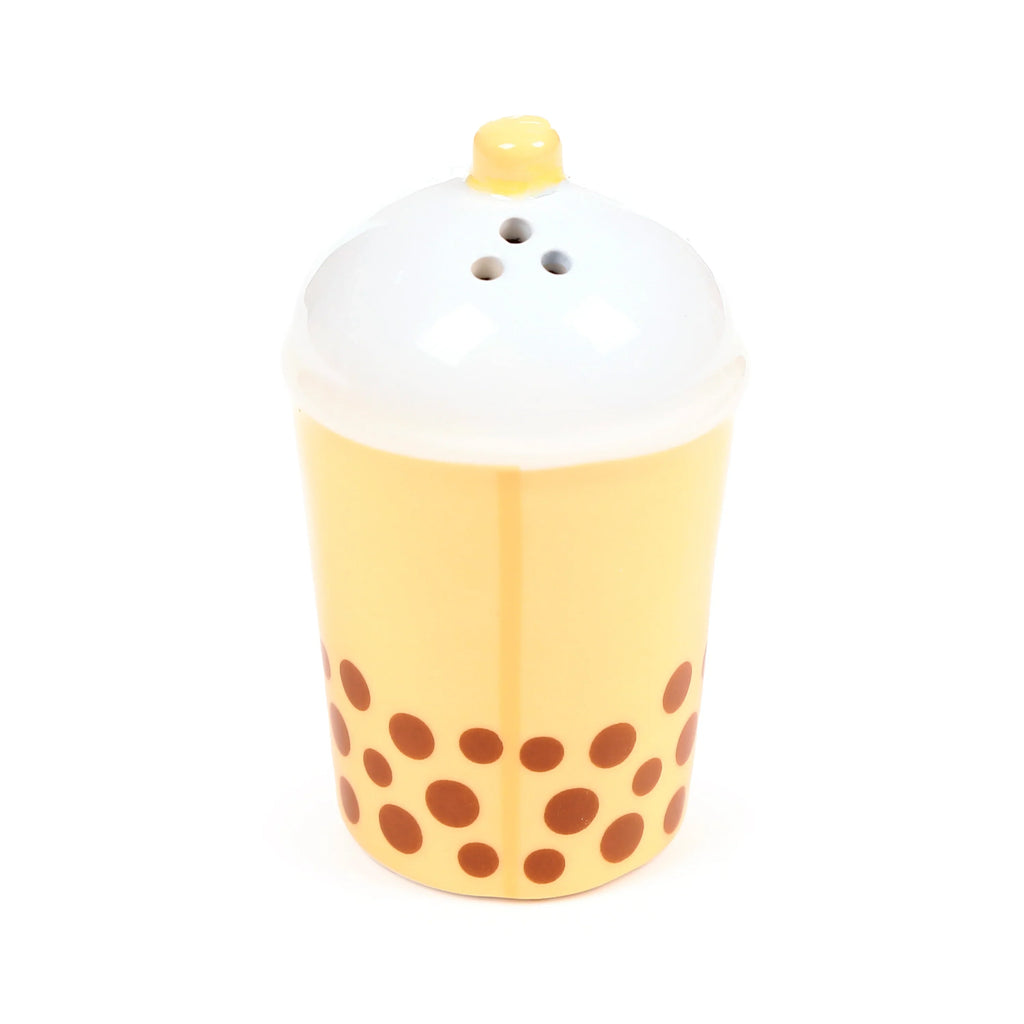 Angled view of a ceramic boba tea salt shaker, light yellow with brown 'pearl' dots and a white foam top featuring three shaker holes and a small yellow straw.