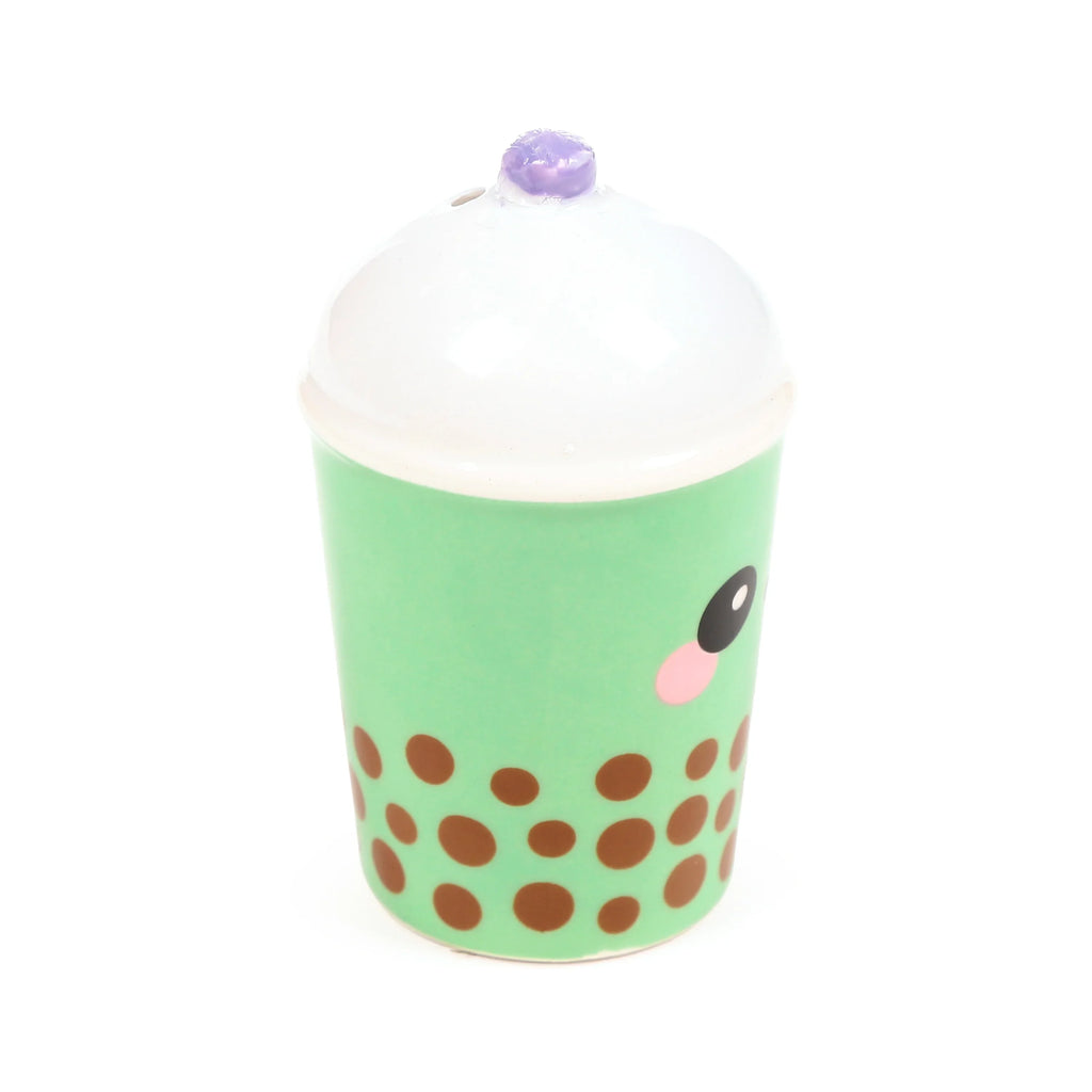 Front view of a ceramic matcha bubble tea shaker, green with brown dots, a white top, and a purple textured detail. It features a black eye and pink cheek.