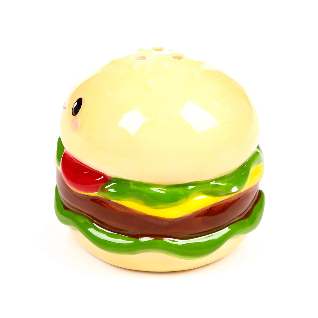 Front view of a ceramic burger-shaped shaker, featuring cream buns, green lettuce, yellow cheese, brown patty, and red sauce. It has a cute black eye with a pink cheek blush and three holes on the top bun.