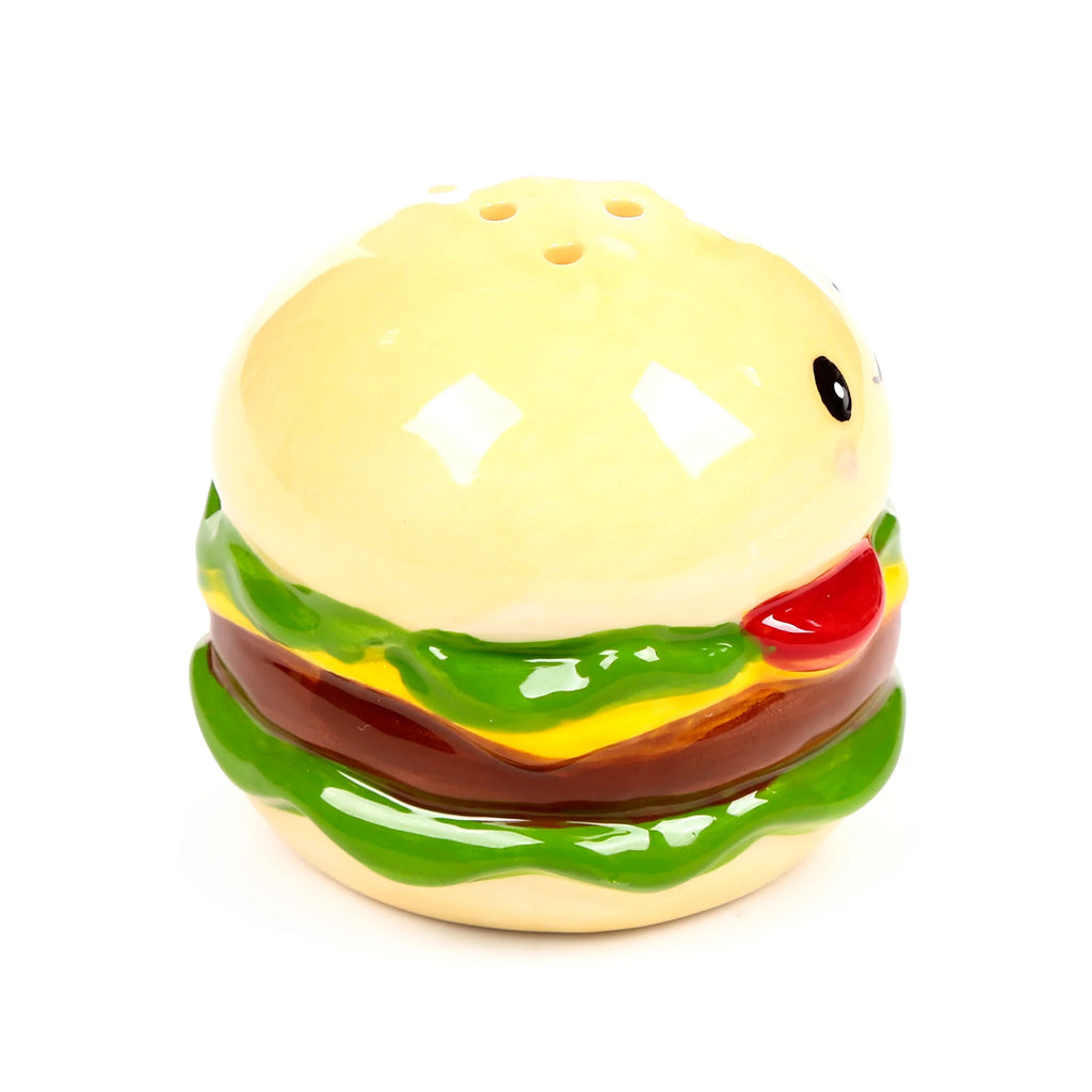 Angled view of a glazed ceramic burger shaker, depicting bun, green lettuce, yellow cheese, brown patty layers, a cute cartoon face, and shaker holes on the top.