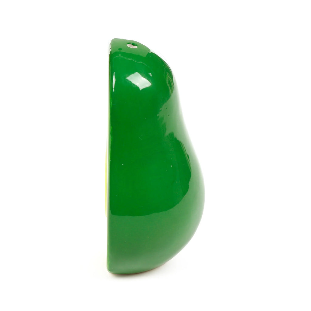 Side profile of a glossy green ceramic avocado half salt or pepper shaker, revealing the lighter yellowish-green sliced interior and a single shaker hole at the top.