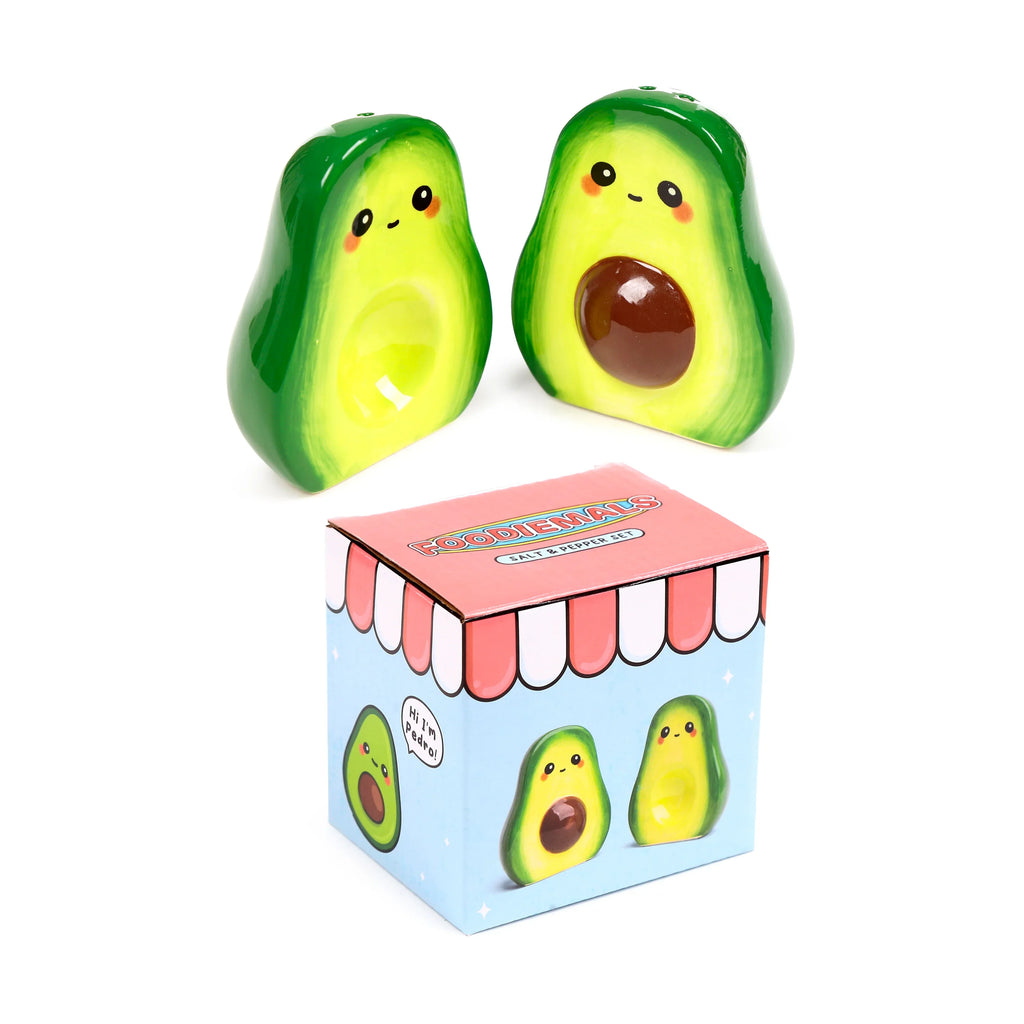 Angled view of two green and yellow ceramic avocado salt and pepper shakers with cartoon faces, one featuring a brown stone, displayed with their light blue and pink illustrated packaging box.