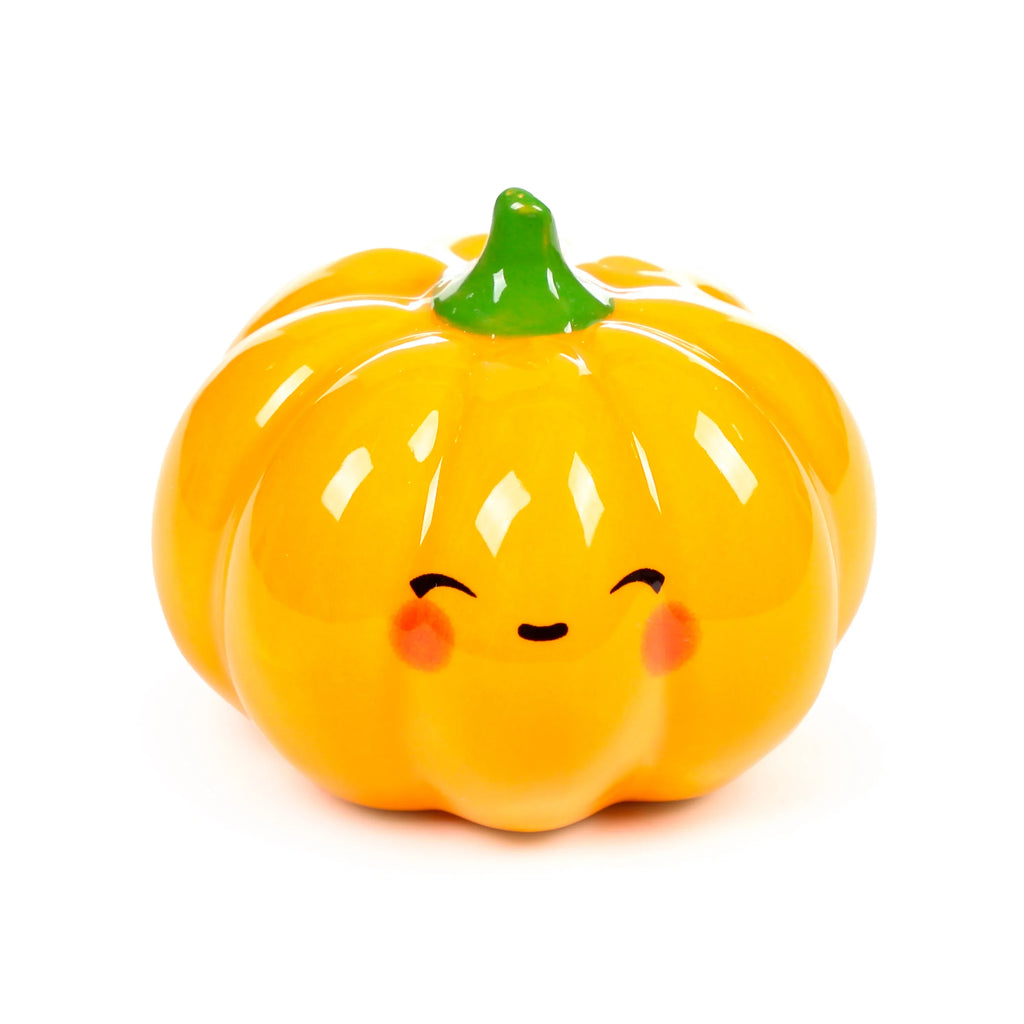 Front view of a glossy, bright orange ceramic pumpkin character with a green stem, featuring a smiling face with small black eyes, a mouth, and rosy cheeks.