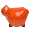 Angled side view of a glossy orange ceramic Highland Coo cow shaker, with white horns, white snout, and dark hooves.