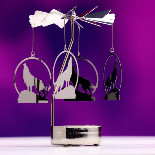Polished silver-coloured metal spinning tea light carousel candle holder, showcasing its four hanging howling wolf silhouettes, reflective fan blades, and round base, on a vibrant purple background.