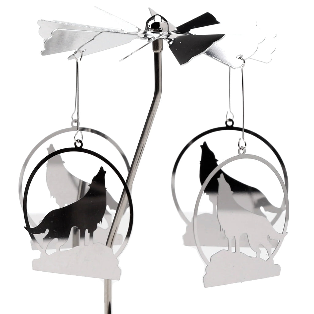 Angled view of a silver-coloured metal spinning tea light carousel candle holder, showcasing its central stem, upper spinning propeller with fan blades, and four hanging circular ornaments each featuring layered howling wolf silhouettes.