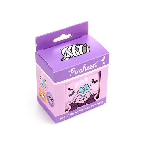 Angled view of a Halloween Pusheen the Cat makeup sponge set in purple and pink packaging, revealing three character makeup sponges through a front window, including Pusheen as a vampire and a ghost. The box also displays 'eek!' text and a mummy Pusheen illustration on its lid.