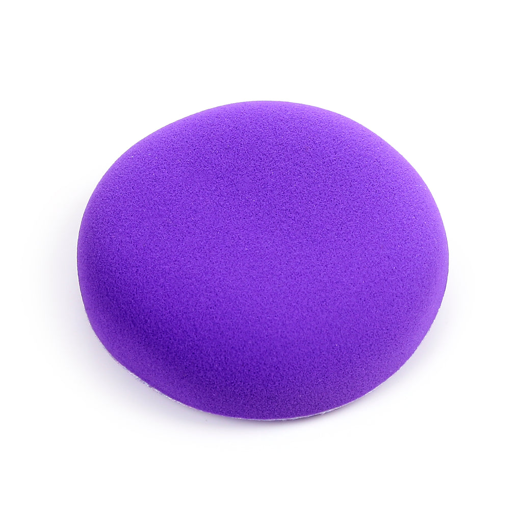 Angled view of a round, vibrant purple beauty sponge with a porous texture, against a white background.