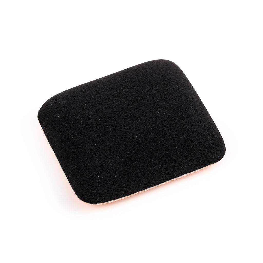 Angled top-down view of a single black rectangular beauty blending sponge, featuring a velvety texture and a visible thin light-coloured edge along the bottom.