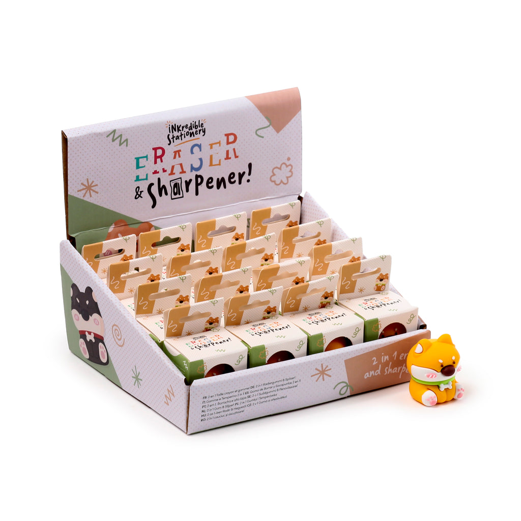 Angled view of a retail display box for 2-in-1 pencil sharpener and eraser sets, showing a black and white Shiba Inu dog graphic. An unboxed yellow Shiba Inu dog pencil sharpener and eraser with a green scarf is placed in the foreground.