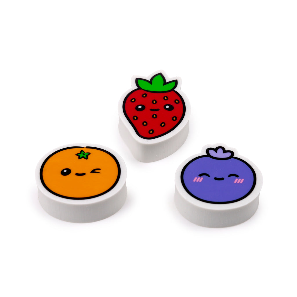 Angled view of a three-piece set of erasers, designed as cheerful fruit characters. The set includes a red strawberry, an orange, and a purple blueberry, each featuring cute cartoon faces and white bases, displayed on a white background.