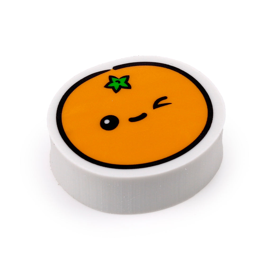 Angled view of a round orange fruit-shaped eraser, featuring a winking cartoon face with a green leaf detail on its top surface and light grey sides, on a white background.