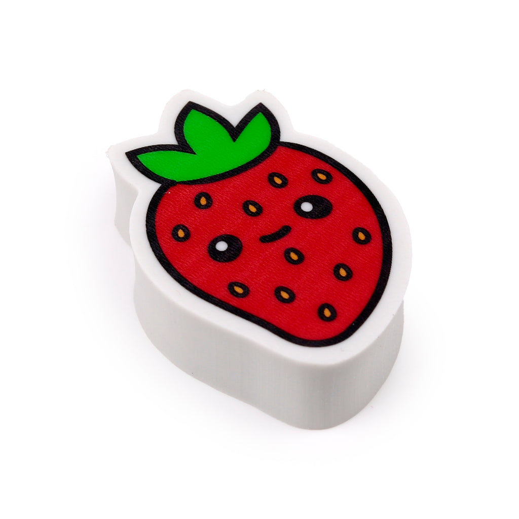 Angled close-up of a red strawberry fruit eraser with green leaves, yellow seeds and a cute cartoon face on a white background.