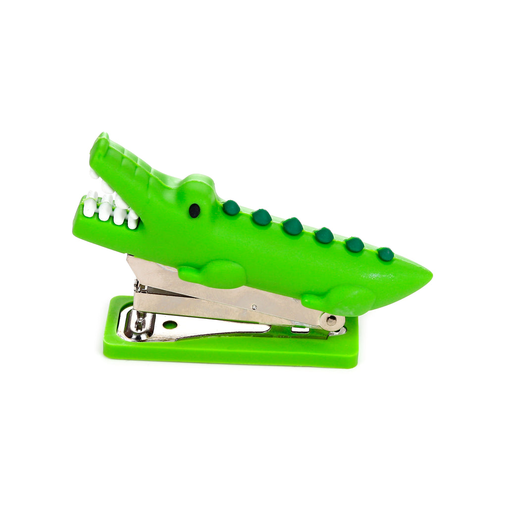 Angled view of a green crocodile mini stapler with an open mouth, showing white teeth and a visible metallic stapling mechanism.