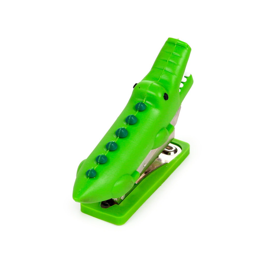 Angled top view of a mini green crocodile-shaped stapler with dark green bumps and black eyes, on a white background.