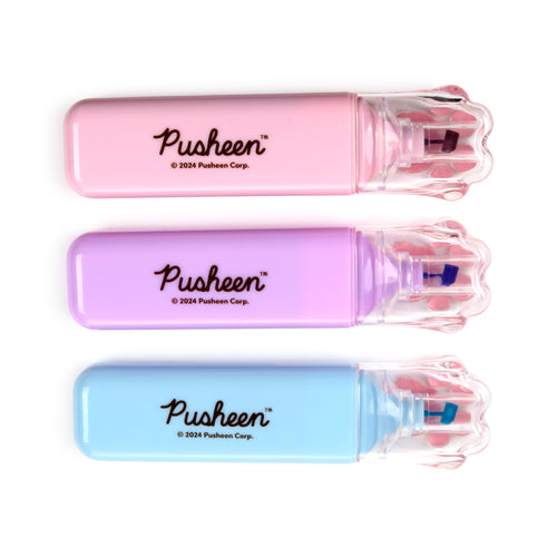 Overhead view of three pastel highlighters in pink, purple, and blue, each featuring a clear cat paw-shaped cap with pink paw pads and the word 'Pusheen' on its barrel, laid horizontally on a white background.