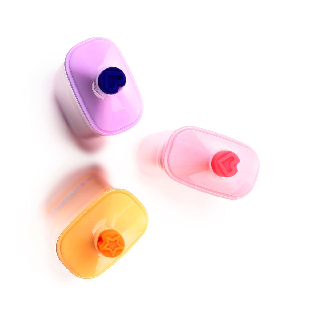 Overhead view of a set of three highlighters on a white background. The purple highlighter has a dark blue heart-shaped cap, the pink highlighter has a red heart-shaped cap, and the orange highlighter has an orange star-shaped cap.