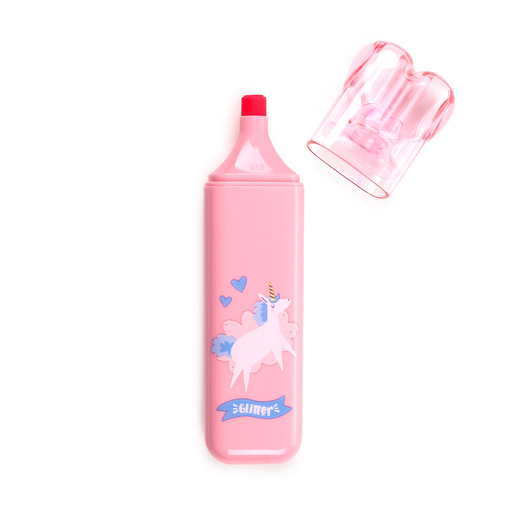 Overhead view of a pink highlighter featuring a white unicorn graphic with a yellow horn, blue mane and tail, set against light blue clouds and two blue hearts. A blue banner with Glitter text is visible below the unicorn, and the translucent pink cap is placed to the side, revealing the red marker tip.