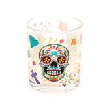 Glass tumbler displaying a vibrant, multi-coloured Day of the Dead sugar skull design, surrounded by scattered diamonds, crosses, and confetti-like patterns.