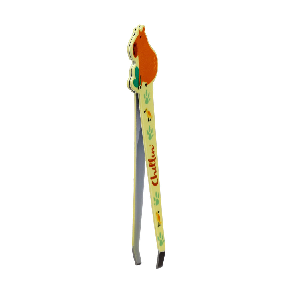 Angled view of pale yellow Capybara shaped tweezers, featuring an orange capybara design, green paw prints, yellow birds, and 'Chillin'' text on one handle.