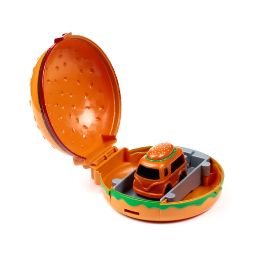 Angled view of an open hamburger-shaped action toy, revealing a small orange truck with a bun on its roof, nestled in a grey launching ramp.