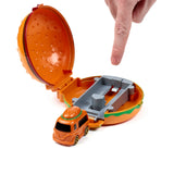 Angled view of an open orange hamburger press & launch action toy, showing its grey launcher mechanism and a small orange hamburger truck, with a hand pointing down.