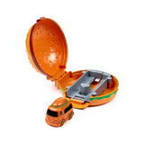 Angled view of an orange hamburger-shaped press and launch action toy. The toy opens to reveal a grey launch track inside, with a small orange toy truck, featuring a bun detail on its roof, positioned in front.