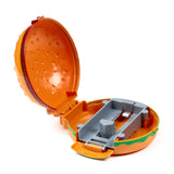 Orange hamburger-shaped press and launch action toy, open at an angle to reveal its grey internal launching mechanism. The toy features textured orange buns with green detailing along the edges.