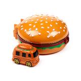 Angled view of an orange, burger-shaped action toy with white sesame seeds, brown patty, green lettuce and red clip details, alongside a smaller orange hamburger truck toy with black windows and yellow wheels, on a white background.