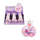 Angled view of a retail display box filled with kids' unicorn water game puzzles, with one individual pink handheld puzzle shown prominently from the front. The toy features a white unicorn head with a colourful rainbow horn, a clear glittery casing containing rings and a small unicorn figure, and pink control buttons.