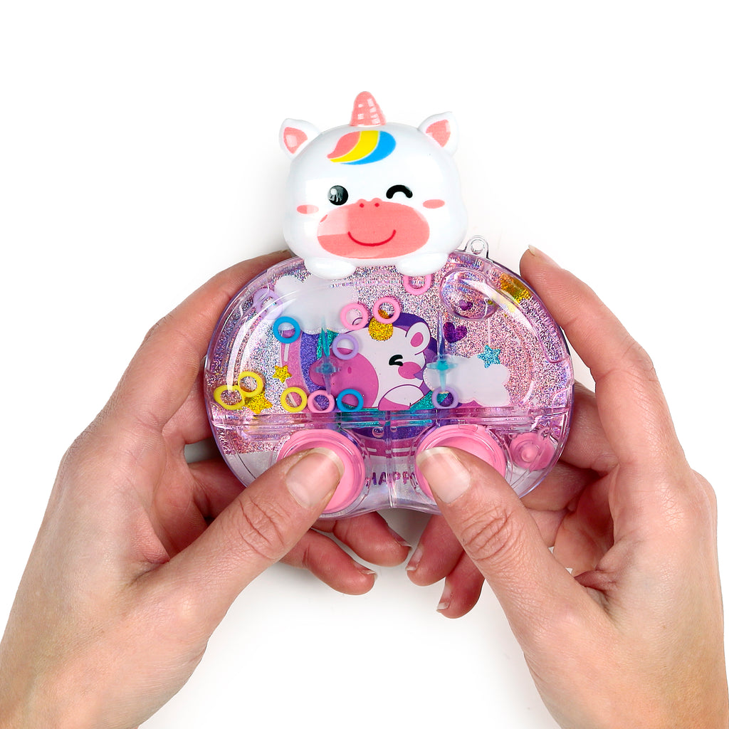 Close-up, hands-on view of a kids unicorn water game puzzle, showcasing its clear, glitter-filled casing with colourful rings, an inner unicorn character, and a white unicorn head, as hands press the pink play buttons.
