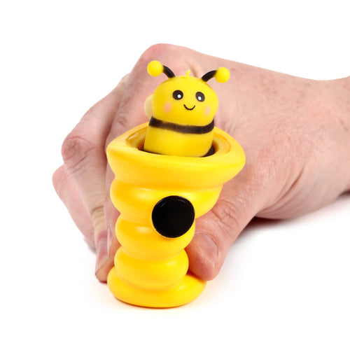 Yellow pop out bee and beehive toy held in a hand, featuring a smiling bee emerging from the ridged yellow base with a black button.