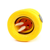 Angled view of a yellow pop-out bee and beehive toy, showing the orange bee's face with black eyes, smile, and cream antennae partially emerged from the ribbed casing.