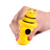 Yellow bee and beehive pop-out toy, pressed by a hand, showing the striped bee with a cute face emerging from its ribbed beehive base, which has a black button.