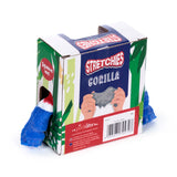 Angled view of a Stretchy Stress Fidget Toy – a Union Jack gorilla – inside its patterned retail box. The blue, red, and white gorilla's limbs protrude from a side cutout. The box features STRETCHIES GORILLA text, a Squeeze me! prompt, green palm leaf patterns, and an illustration of hands stretching a gorilla.
