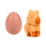A pale peach hatching egg toy and a light brown capybara toy with darker brown feet and snout, featuring closed eyes, displayed side-by-side.