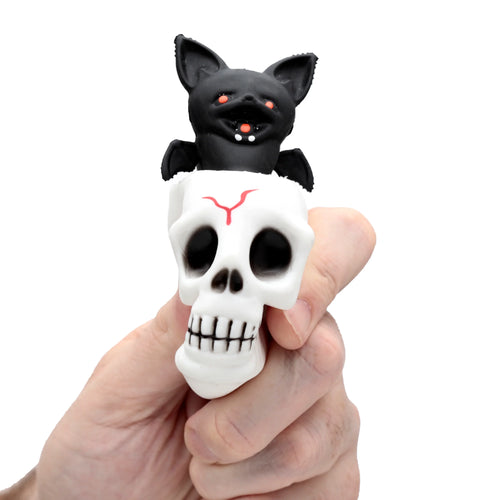 Close-up of a Kids Pop Out Toy - Skull Bat, held in a hand. A black bat with red eyes and fangs emerges from a white skull with a red forehead design.