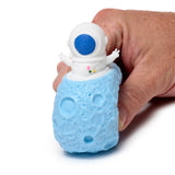 Close-up of a hand holding a white spaceman astronaut figure, with a blue visor and small multicoloured details, emerging from a textured blue planet pop out toy.