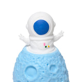 Close-up of a white spaceman astronaut pop out toy with a blue visor and colourful suit details, one hand raised in a peace sign, emerging from a light blue, cratered planet base.