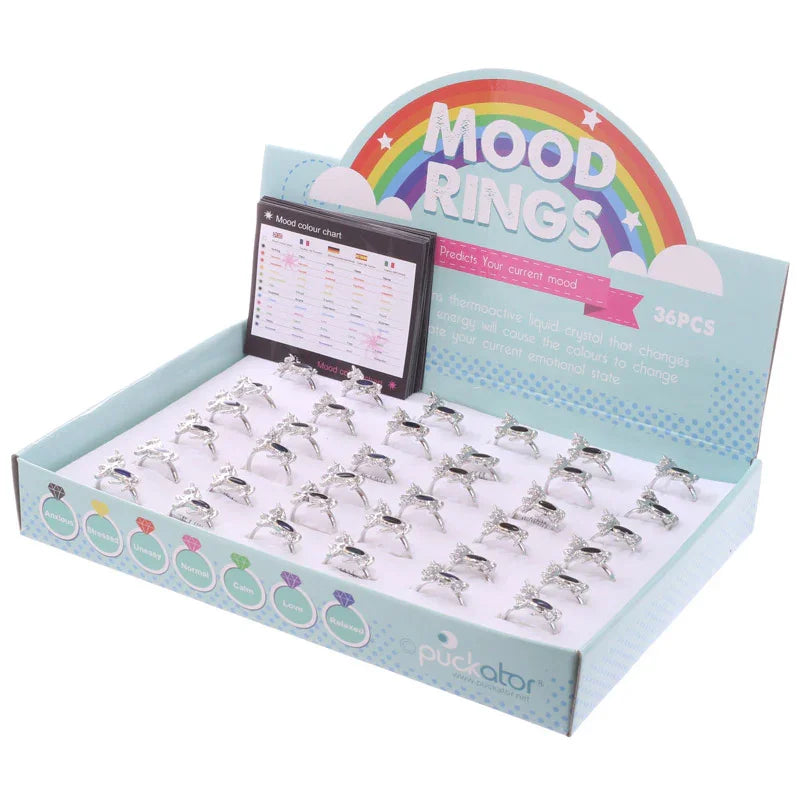 Angled view of a light blue retail display box filled with numerous silver-coloured Funky Unicorn Design Mood Rings. Each ring features a dark, mood-sensitive element. The display box includes a 'Mood Rings' rainbow header, a mood colour chart, and text explaining mood prediction, indicating 36 pieces.