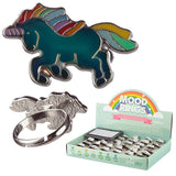 A top view of a unicorn mood ring with a colour-changing teal body and rainbow mane, horn, and tail, shown alongside an underside view revealing its silver adjustable ring band, and an angled view of a retail display box containing multiple mood rings.