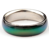 Angled close-up of a Mood Ring with a silver-coloured inner band and an outer surface displaying a colour shift from dark blue to green.