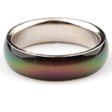 Angled close-up of a mood ring with a metallic silver-coloured band, displaying a shifting spectrum of iridescent green, yellow, and purple.