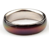 Angled close-up of a mood ring with a glossy outer band displaying a gradient of dark green, orange, red, and deep purple hues, and a metallic silver-coloured inner band.