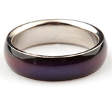 Close-up, angled view of a broad-banded mood ring, showing its iridescent deep purple and reddish-brown outer surface and polished silver-coloured inner band.